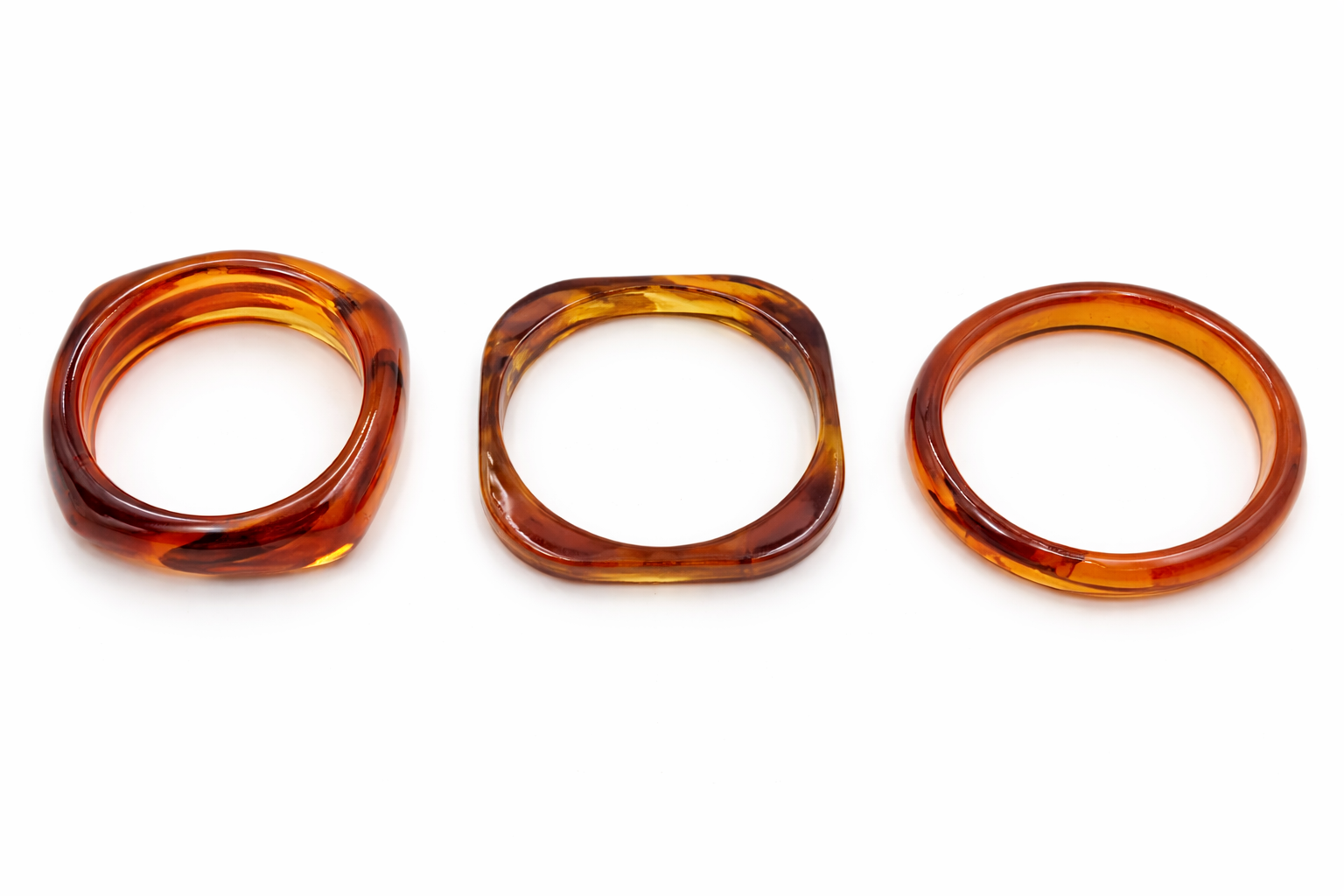 Pack de 3 pulseras rígidas de resina efecto carey ámbar en diferentes formas, sobre fondo blanco